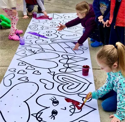 Niños pintando juntos un mural de papel en el piso